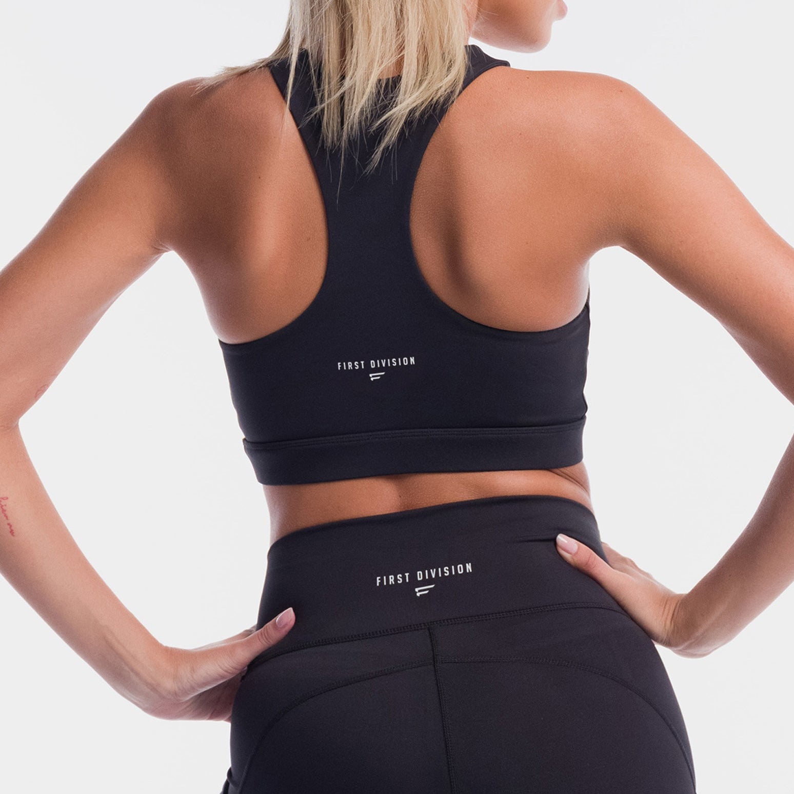 Person wearing a black sports bra and leggings with 'First Division' branding on a white background